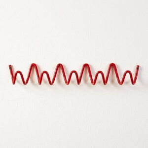 May include: A red metal wall hook with a wavy design. The hook is mounted on a white wall. The hook is approximately 24 inches long.
