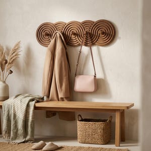 Può includere: Appendiabiti in legno con un design a spirale, che tiene un cappotto color cammello e una borsa rosa. Sotto, una panca in legno con un cesto intrecciato, una coperta e delle pantofole. Vaso decorativo con piante essiccate.