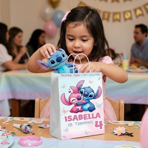 A young girl with a pink hair bow sits at a birthday party table, smiling as she pulls a blue Stitch plush toy out of a personalized party favor bag. The white paper bag features a custom design with the characters Stitch and Angel, reading "THANK YOU FOR COMING" and "ISABELLA IS TURNING 4". The background shows a softly blurred festive party setting with guests and a "HAPPY BIRTHDAY" banner.