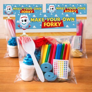 A front view of several clear plastic bags with Toy Story-themed bag toppers. Each topper is blue with a wood grain bottom edge and features a Forky character. The yellow and red block text reads, "MAKE YOUR OWN FORKY." The bags are filled with various small items, including a white plastic fork, colorful candy-like sticks, googly eyes on a card, rolled-up blue elements, and a small white cup. The bags are lined up on a wooden table.