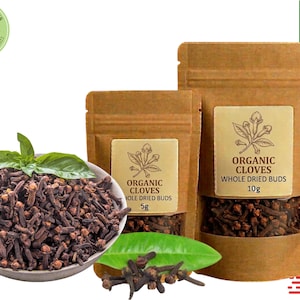 Può includere: Immagine con chiodi di garofano biologici. Una ciotola bianca contiene chiodi di garofano interi essiccati, completati da foglie verdi fresche. Due sacchetti di carta marrone mostrano etichette con il testo "Organic Cloves" e "Whole Dried Buds", con pesi di 5g e 10g.