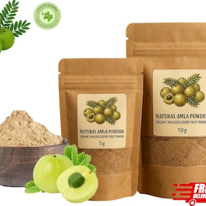May include: Two brown kraft paper pouches of Natural Amla Powder labeled 5g and 10g, a wooden bowl filled with light brown powder, and several fresh green Indian gooseberry fruits with small leaves, all displayed against a white background.