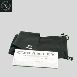 May include: A black microfiber cleaning cloth and drawstring pouch with the Oakley logo. A white card with the Oakley logo and text is also included. The items are likely for eyewear.