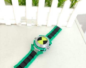 May include: A wrist-worn device featuring a circular silver-colored face with a bright lime green and black hourglass-shaped center. The band is constructed from interlocking teal and black segments, creating a segmented, blocky appearance.