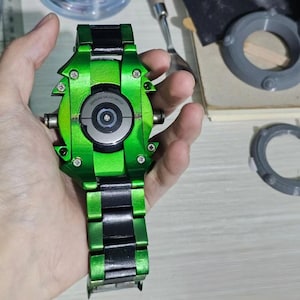 May include: A smartwatch with a metallic green custom housing featuring exposed silver screws and a black link bracelet. The circular back sensor area is clearly visible with the text Samsung Galaxy Watch printed around the central glass component.