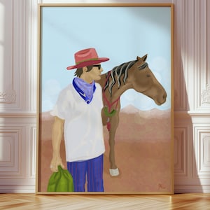 May include: A framed art print depicting a person in a red hat and sunglasses, with a blue bandana, standing beside a brown horse. The person holds a green bag. The background shows a light blue sky and a brown landscape.