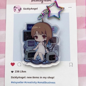 May include: An acrylic keychain featuring a cartoon character with brown hair sitting among several computer monitors and cables. The keychain has a rainbow-colored star-shaped clasp and is displayed on a printed card resembling an Instagram post.