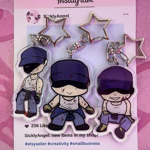 May include: Three acrylic keychains featuring cartoon characters in blue caps, white tank tops, and blue jeans. Each keychain has a silver star-shaped top. The Instagram post reads "SicklyAngel: new items in my shop!"