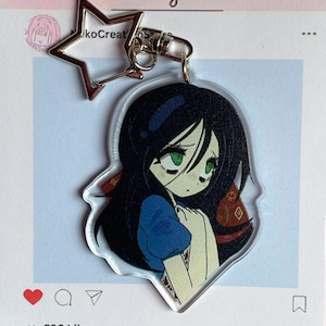 Puede incluir: Un llavero acrílico transparente con una ilustración de estilo anime de una niña con cabello negro y ojos verdes. El llavero tiene un cierre plateado en forma de estrella. La publicación de Instagram muestra el texto "NekoCreationStore: new items in my shop!"