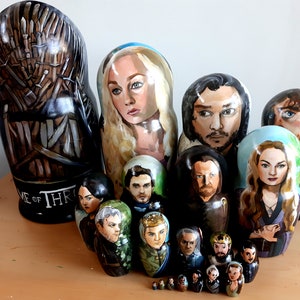 May include: A set of hand-painted wooden nesting dolls featuring characters from the popular TV show Game of Thrones. The largest doll depicts the Iron Throne, and the smaller dolls feature characters like Daenerys Targaryen, Jon Snow, and Sansa Stark.