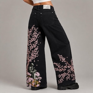 May include: Black denim wide-leg jeans with a pink cherry blossom and knight illustration. The jeans have a high waist and a button and zip closure. The Urban Outfitters label is visible on the back.