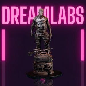 Puede incluir: Estatua de una figura con equipo táctico, sosteniendo un arma, sobre una base con calaveras y una bolsa de lona. Un rifle descansa sobre la bolsa. La palabra "DREAM LABS" se muestra en letras rosas arriba.