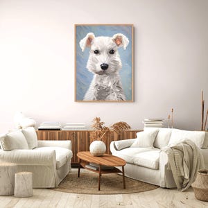 May include: A framed wall art print featuring a portrait of a white dog with textured fur, dark eyes, and a black nose, set against a light blue brushstroke background. The artwork is displayed in a light wood frame on a plain wall.