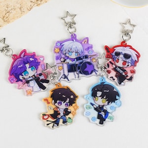 Puede incluir: Cinco llaveros de personajes de estilo anime con cierres en forma de estrella. Cada llavero presenta un personaje diferente con un tema musical, con colores vibrantes como morado, rojo, azul y naranja. Los personajes tocan instrumentos como batería, guitarra y teclado.