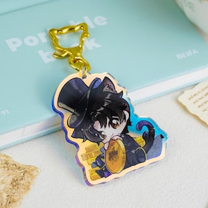 May include: An acrylic keychain featuring a cartoon character with black cat ears and a top hat, holding a gold coin while sitting on a pile of gold. The charm is attached to a gold-colored metal cat-shaped clasp and has a holographic finish.