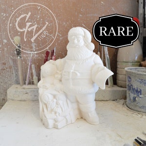 May include: White ceramic figurine of Santa Claus holding a bag of toys. The figurine is marked "RARE" and "Made in the USA".