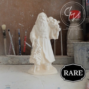 May include: White ceramic figurine of Santa Claus holding a Christmas tree and a bag of gifts. The figurine is made by Grapevine Ceramics & Gifts and is marked "Made in the USA" and "1998".