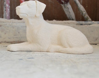 Könnte beinhalten: Weiße Keramikskulptur eines liegenden Hundes. Der Hund ist nach links gerichtet und hat den Kopf angehoben.