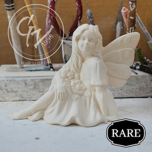 May include: A cream-colored ceramic fairy figurine with long flowing hair, wings, and a floral design on the dress. The fairy is seated with one leg extended. The word "RARE" is in a black and white frame.