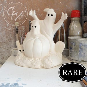 Könnte beinhalten: Weiße Keramik-Halloween-Figur aus zwei Geistern, die einen Kürbis halten. Die Figur ist mit "Made in the USA" und "GV 1998" gekennzeichnet. Das Wort "RARE" ist in Schwarz auf weißem Hintergrund geschrieben.