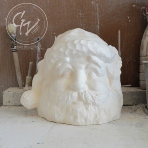 Pode incluir: Escultura de cerâmica branca da cabeça do Papai Noel com barba e uma coroa no chapéu. A escultura está inacabada e tem uma textura áspera.