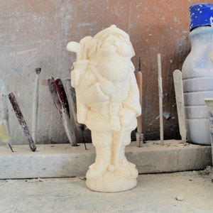 May include: White ceramic figurine of a golfer wearing a hat and carrying a golf bag. The figurine is standing on a wooden base.