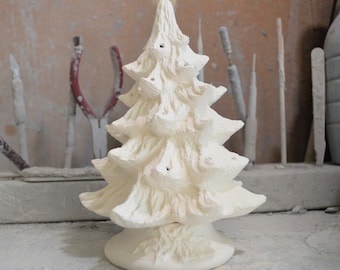May include: White ceramic Christmas tree ornament with a textured surface and a base. The tree has a traditional shape with multiple tiers and is ready to be decorated.