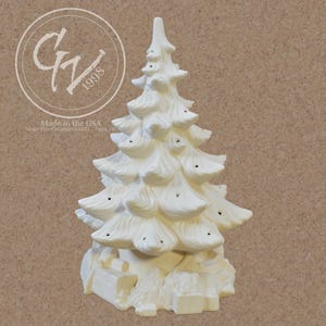 May include: A white ceramic Christmas tree with a textured surface, featuring multiple tiers of branches and small holes for lights. The tree is decorated with presents at the base. The text "Made in the USA" is visible.