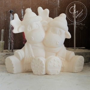 May include: White ceramic moose figurine with a winter theme. The moose are wearing hats and scarves and have a sweet expression on their faces. The figurine is ready to be painted.