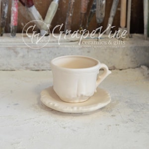 May include: A white ceramic teacup and saucer set. The cup has a fluted design and a handle. The saucer has a scalloped edge.