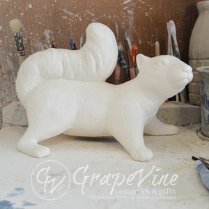 May include: White ceramic squirrel figurine with a bushy tail. The figurine is standing on a white surface. The figurine is a blank canvas ready to be painted.