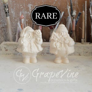 May include: Two white ceramic Santa Claus figurines, each holding a bag of gifts. The figurines are standing on a white surface. The word "RARE" is written in black letters on a black background.