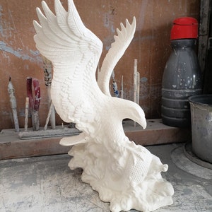 May include: White ceramic sculpture of an eagle with its wings spread, holding a fish in its talons. The eagle is perched on a rocky base.