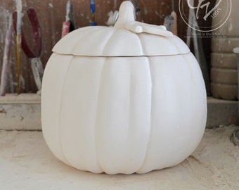 May include: White ceramic pumpkin shaped container with a lid. The container has a smooth, rounded surface and a slightly textured lid. The lid has a small handle on top. The container is made in the USA.