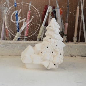 Może przedstawiać: Biała ceramiczna figurka choinki z kokardą i prezentami. Figurka jest nieukończona i gotowa do pomalowania.