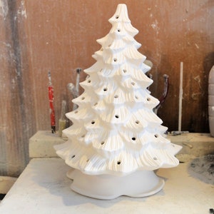Puede incluir: Árbol de Navidad de cerámica blanca con una superficie texturizada y agujeros para luces. El árbol está sobre una superficie blanca.