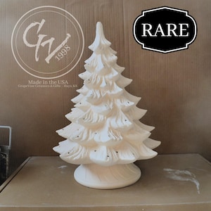 Può includere: Un albero di Natale in ceramica color bianco crema. L'albero ha più livelli di rami ed è montato su una base rotonda. La parola "RARE" è in un'etichetta in bianco e nero. È visibile anche il testo "Made in the USA".