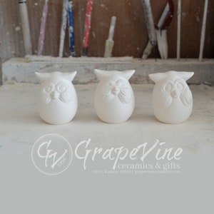 May include: Three white ceramic owl figurines with detailed facial features. The owls are sitting on a light gray surface.