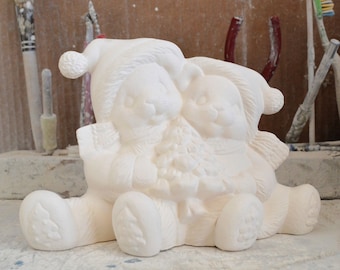 May include: White ceramic figurine of two bears holding a Christmas tree. The bears are wearing hats and scarves.
