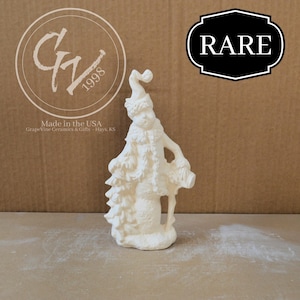 Puede incluir: Una figura de cerámica blanca de Papá Noel con un abrigo largo, sombrero y bastón. La figura está de pie sobre una pequeña base. La palabra "RARE" está en una etiqueta en blanco y negro. También se ve el texto "Made in the USA".