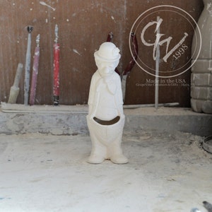 Puede incluir: Figura de cerámica blanca de un payaso con una gran sonrisa y un sombrero. El payaso lleva una camisa y pantalones con un bolsillo. La figura está hecha en los Estados Unidos por GrapeVine Ceramics & Gifts - Hays, KS.