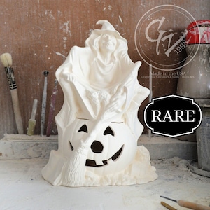 May include: White ceramic Halloween figurine of a witch riding a jack-o'-lantern. The witch is wearing a pointed hat and holding a broom. The jack-o'-lantern has a carved face and a lit candle inside. The figurine is marked "RARE".