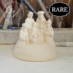 May include: A cream-colored ceramic nativity scene featuring figures of the Holy Family and the Three Wise Men. The base is round, and the figures are detailed. The word "RARE" is in a black and white badge. The text "Made in the USA" is visible.