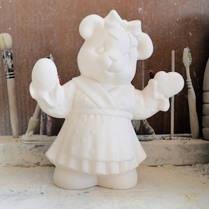 Può includere: Figurina di orso in ceramica bianca che indossa un vestito con un motivo a stelle. L'orso ha un fiocco nei capelli e tiene un cuore in mano.