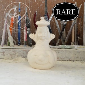 May include: A white ceramic figurine of a girl dressed in a pumpkin costume. The girl is wearing a white hat and has a smiling face. The figurine is labeled "RARE".