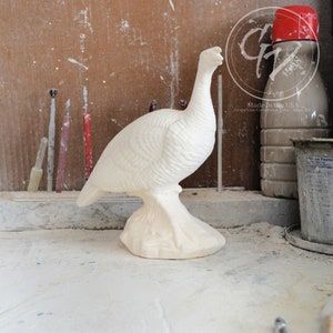 May include: White ceramic turkey figurine with a detailed design. The figurine is standing on a base and has a long neck. Made in the USA. Grapevine Ceramics Gifts, Havelock, KS.