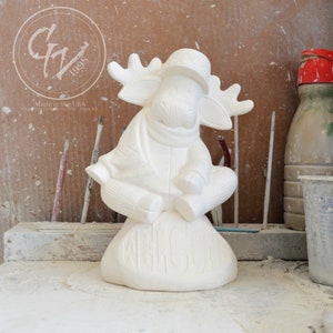 May include: White ceramic moose figurine wearing a hat and scarf, sitting on a rock with the word "Welcome" carved into it.