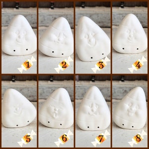 May include: Eight white ceramic candy corn shaped ornaments with different facial expressions. The ornaments are arranged in two rows of four. Each ornament has a small hole at the bottom for hanging.