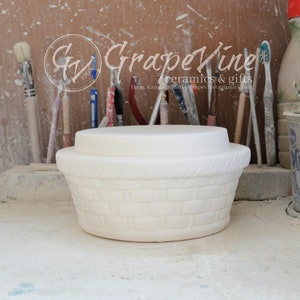 May include: White ceramic basket with a lid, featuring a woven design. The basket is unfinished and ready to be painted.