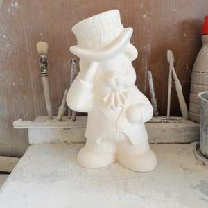 Könnte beinhalten: Weiße Keramikfigur eines Bären, der einen Hut mit Sternen und Streifen trägt. Der Bär trägt eine Jacke und eine Hose. Die Figur ist bereit zum Bemalen.